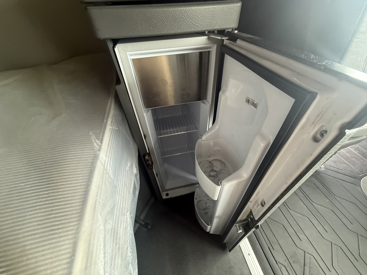 Vehicle interior showing a small refrigerator/freezer unit with open door and empty shelves inside a Volvo VNR64T660 truck sleeper area.
