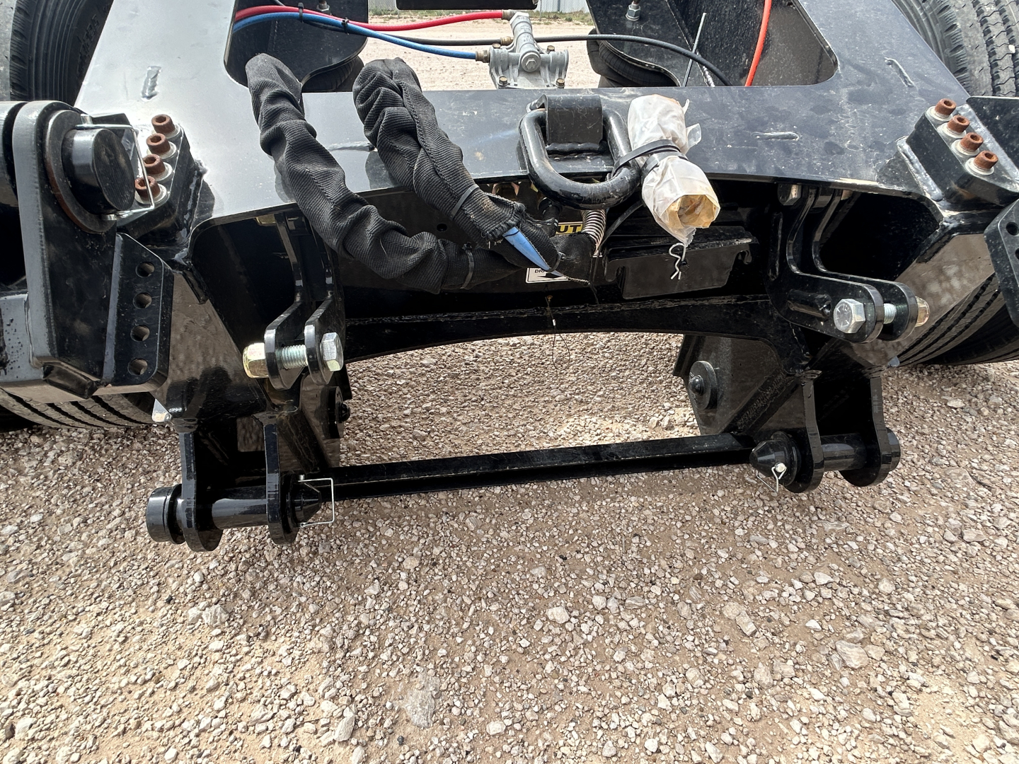 Trailer chassis and flip axle assembly showing mounting hardware and hydraulic lines with black frame and exposed bolts.