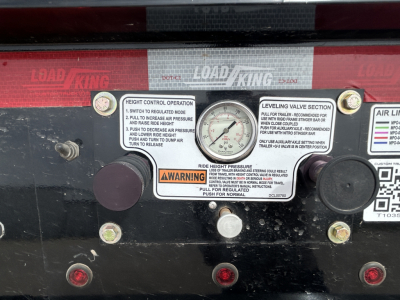 Load King equipment control panel with height gauge, leveling valve, and warning labels on a black metal surface; includes dials and stickers.