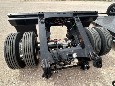Load King flip axle trailer chassis showing dual rear axles, hydraulic lines, and wiring harnesses; components mounted on steel frame with black paint.