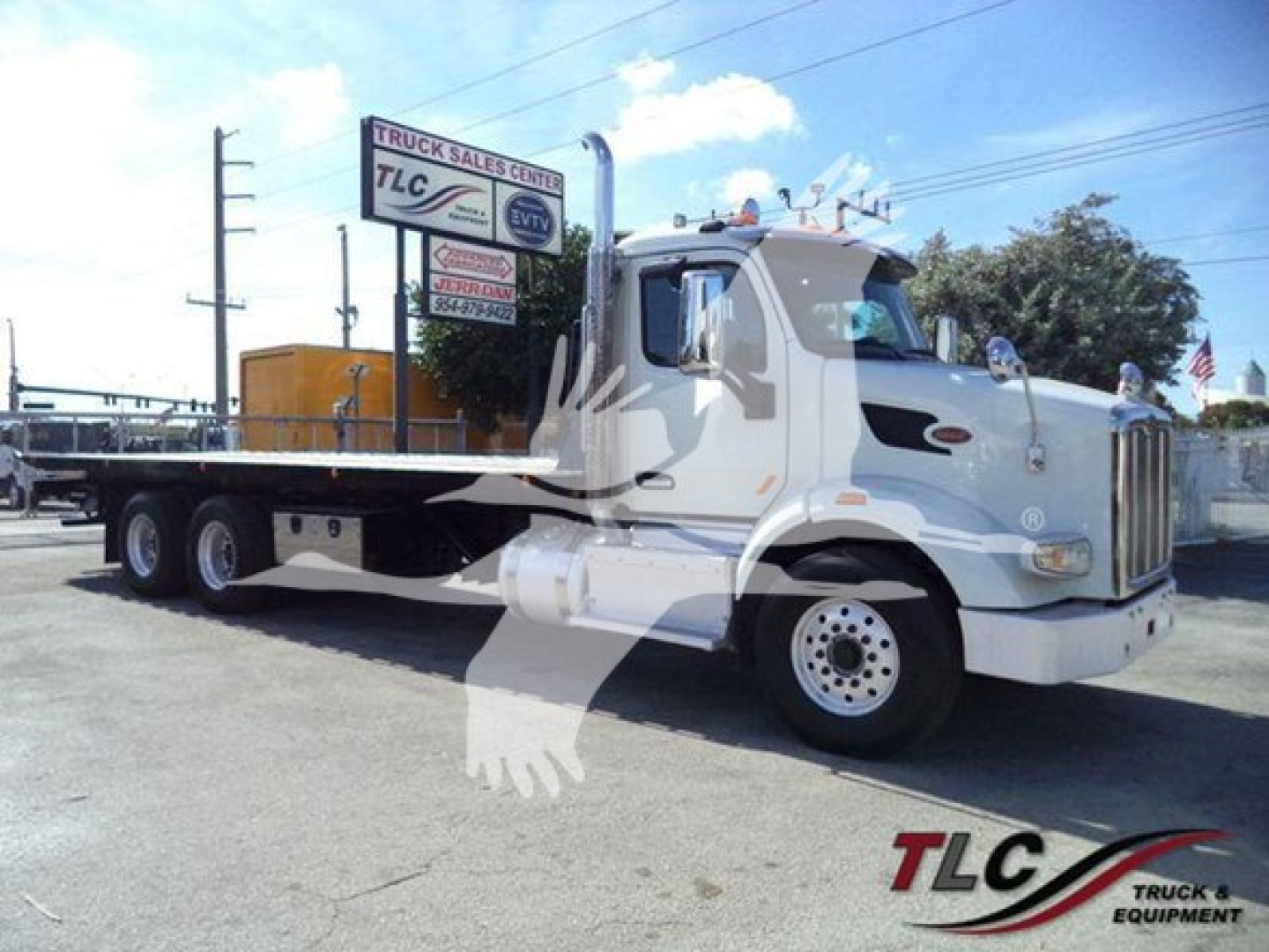 Peterbilt 567 rollback truck in view showing front and side with white cab and flatbed, dealership lot in background.