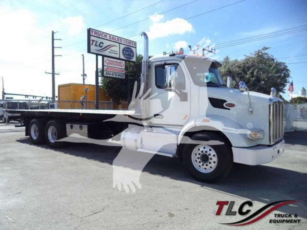 Peterbilt 567 rollback truck in view showing front and side with white cab and flatbed, dealership lot in background.
