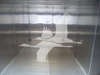 Image shows the interior of a metal trailer or container with a faint graphic of two birds in flight on the far wall.