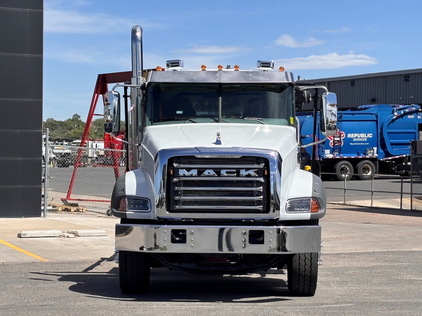 Front view of a white 2027 Mack GR64B truck showing large grille with MACK badge, chrome bumper, dual headlights, and vertical exhaust stacks.