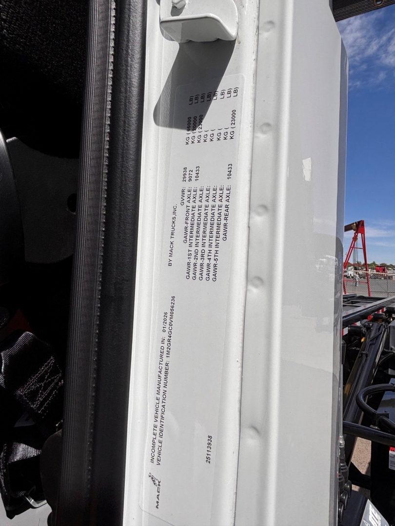 Label sticker on vehicle door frame with small printed text and numbers, part of a Mack GR64B roll-off truck showing VIN area and serials.