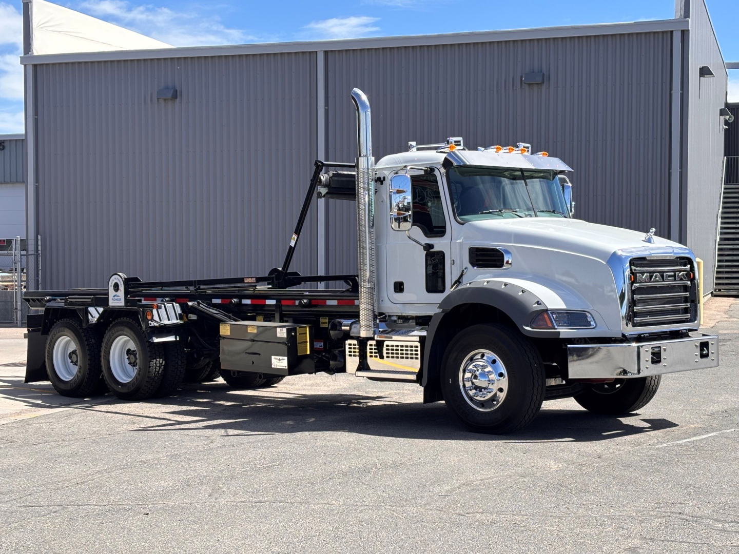 Mack GR64B Roll-off truck in side view showing chassis, cab, and tipper mechanism with chrome exhaust stacks and dual rear axles.