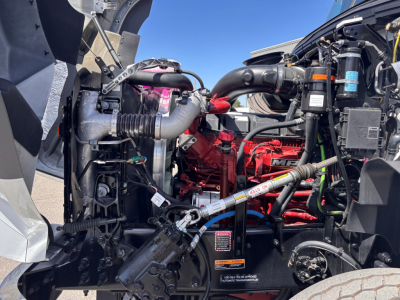Engine bay of a new 2027 Mack GR64B rolloff truck showing red engine block, hoses, and components including air intake and coolant lines.