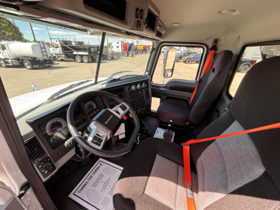 Truck cab interior showing steering wheel, dashboard gauges, and driver seat with red seat belt in a new Mack GR64B roll-off truck.