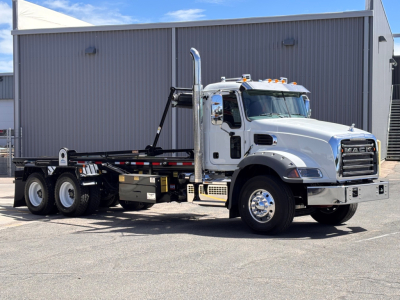 Mack GR64B Roll-off truck in side view showing chassis, cab, and tipper mechanism with chrome exhaust stacks and dual rear axles.