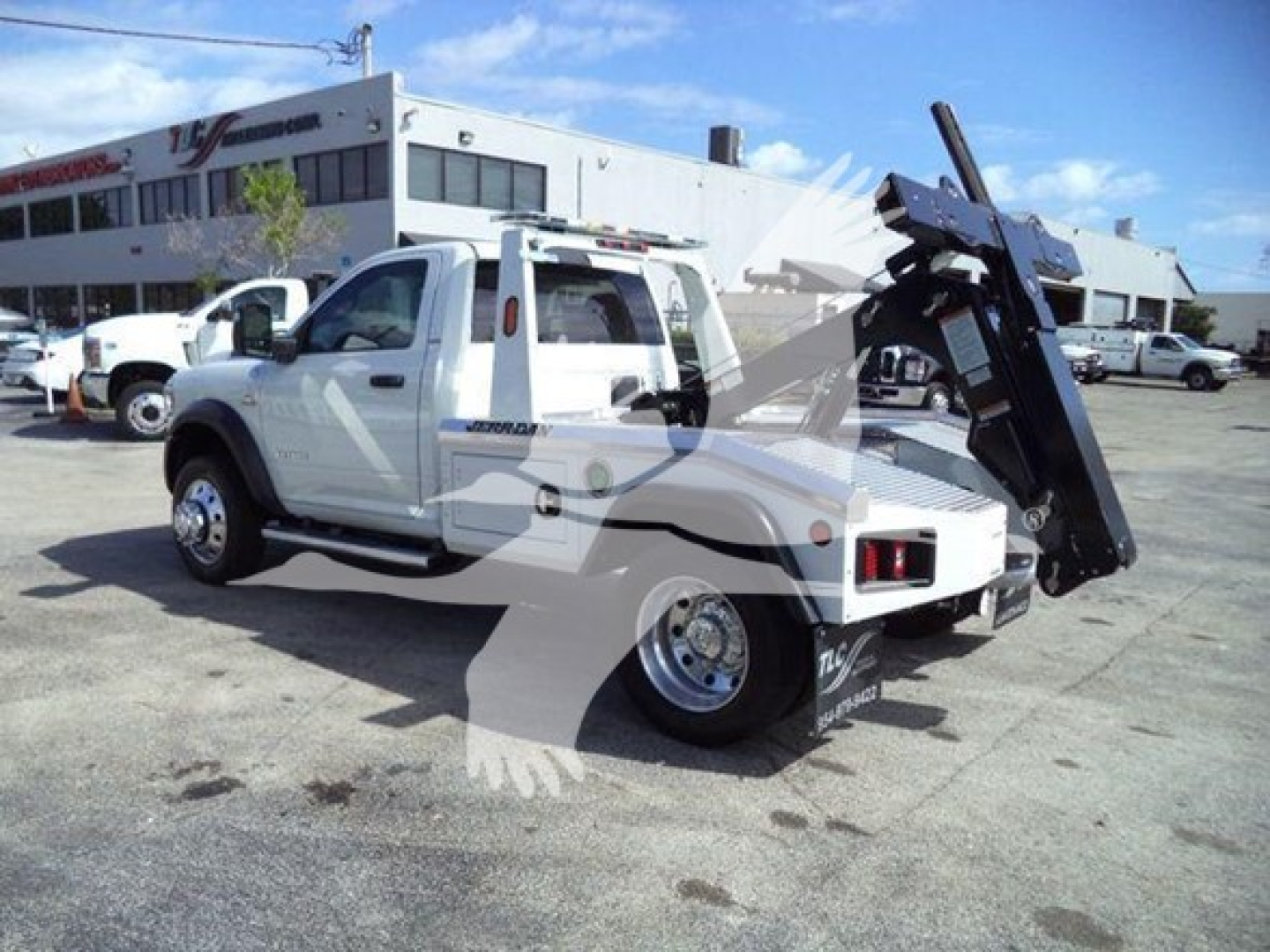 Ram 4500 flatbed tow truck with winch arm in rear, white cab, large dual rear tires, dealership lot in background.