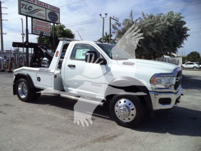 Ram 4500 SLT tow truck with winch equipment in a dealership lot. Side view shows white cab, flatbed, chrome wheels, RAM badge on door, TLC and other signage in background.