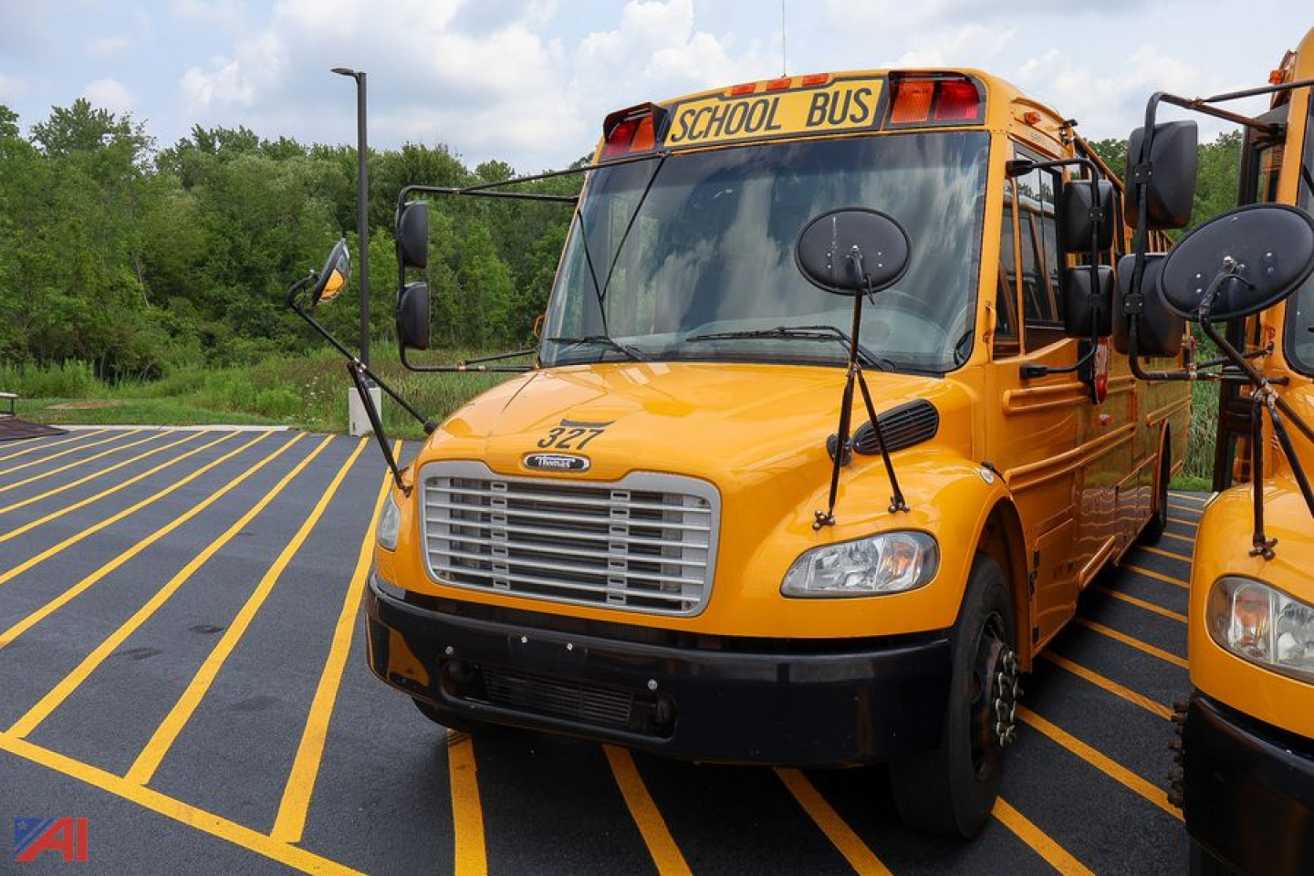 Yellow Freightliner Thomas Saf-T-Liner school bus in a parking lot, front view with extended mirrors and School Bus sign on top.