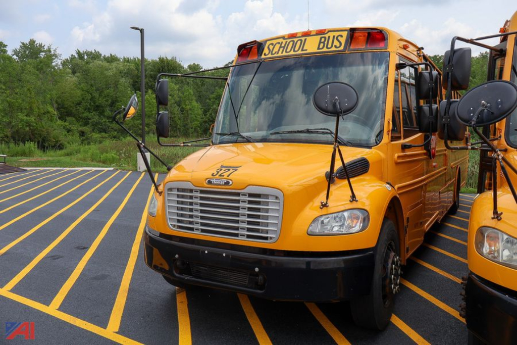 Yellow Freightliner Thomas Saf-T-Liner school bus in a parking lot, front view with extended mirrors and School Bus sign on top.