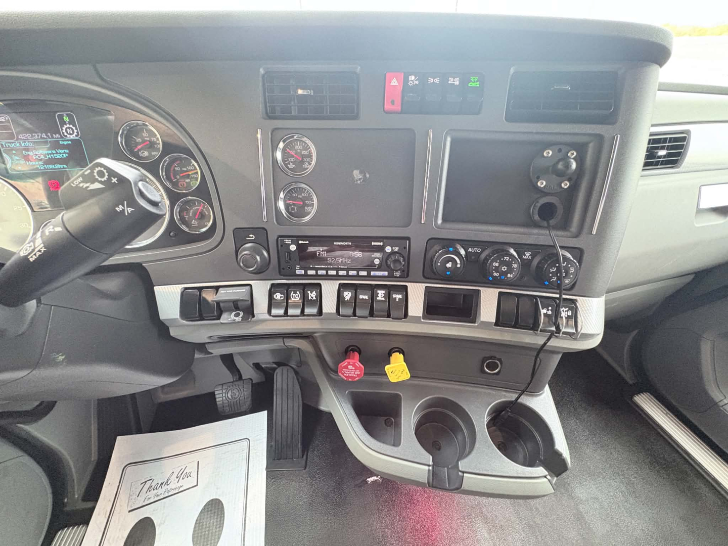 Dashboard and center console of a Kenworth T680 truck cab showing gauges, control switches, ignition area, and cup holders.