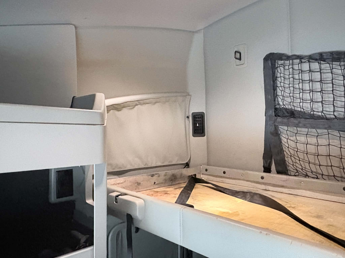 Kenworth T680 sleeper cab interior glimpse showing upper bunk and side storage with netting and seatbelt strap.