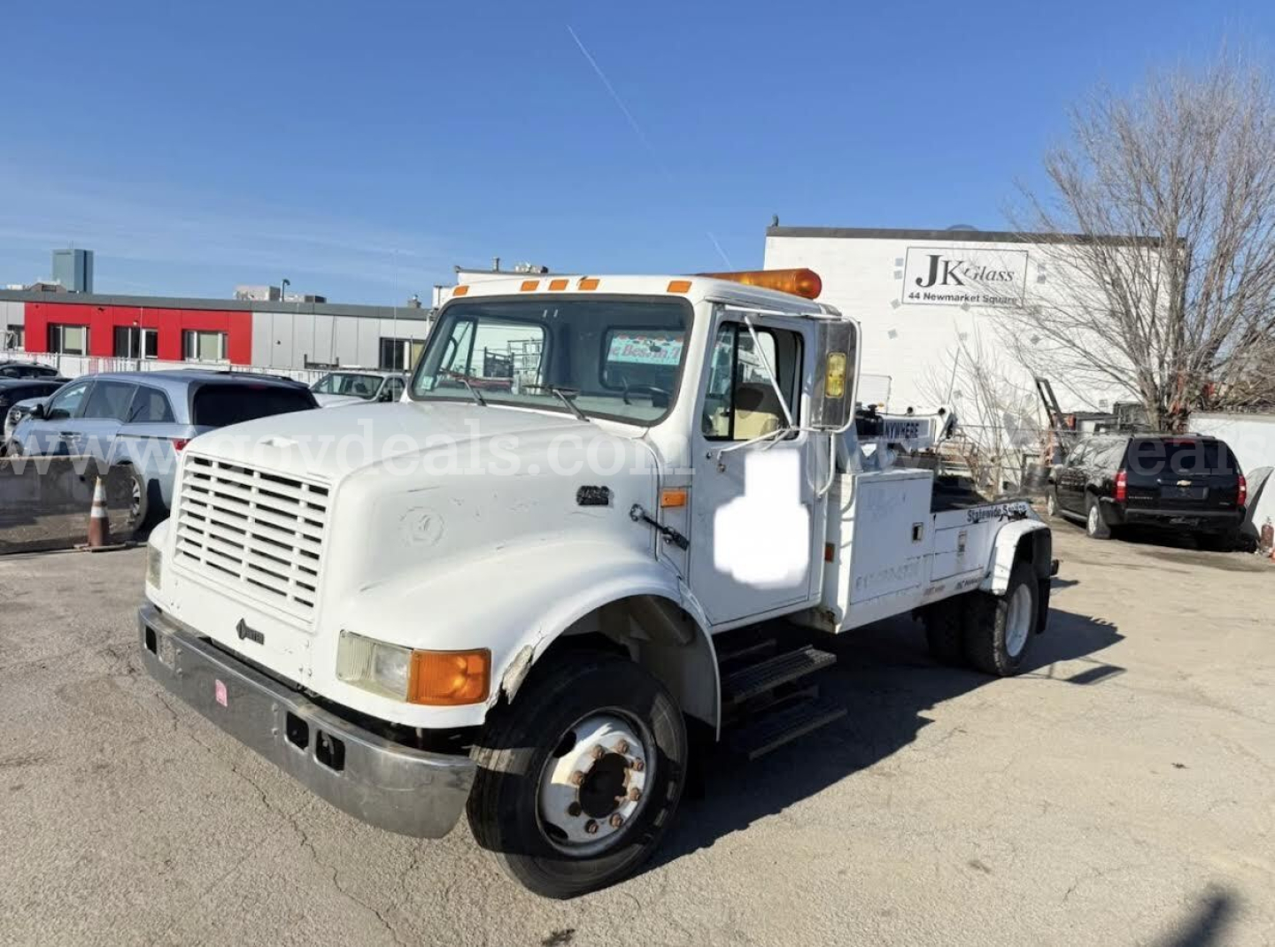 International 4700 tow truck front-left side view showing towing bed and cab with orange beacon lights