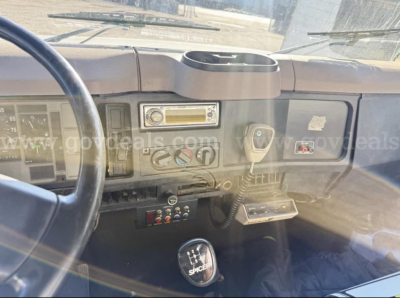 Truck cab dashboard of 1996 International 4700 showing steering wheel, radio, climate controls, gear shifter, and 5-speed manual shifter knob