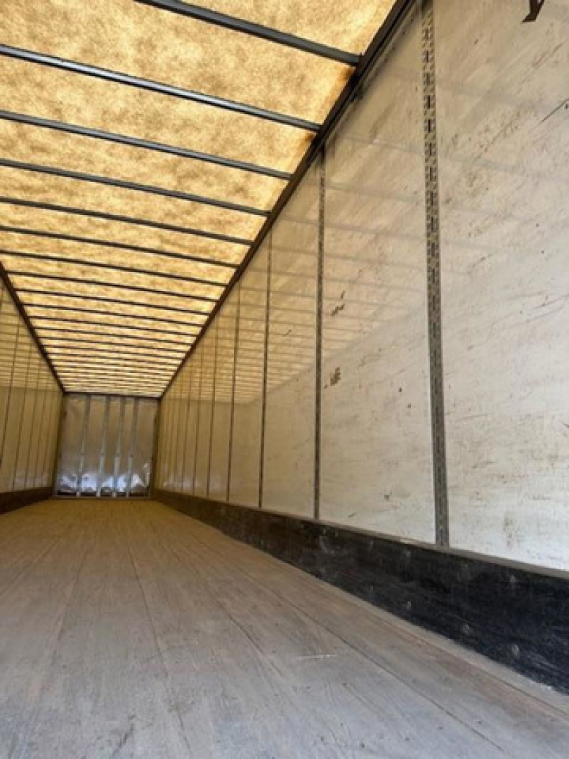 Van trailer interior showing empty cargo bay with wooden floor, side walls, and overhead support beams.