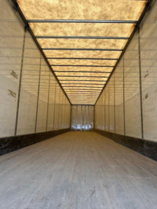 Trailer interior showing long cargo area with wooden floor, light panels along sides, and ceiling translucent panels.