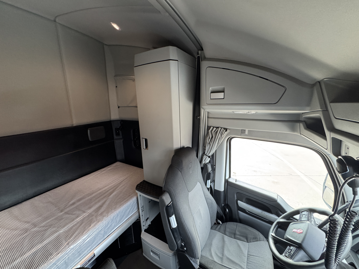 Kenworth truck interior cabin with sleeper berth and captain chair; dashboard and steering wheel visible.