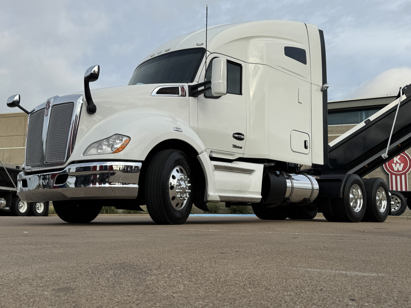Kenworth T680 conventional sleeper truck side view showing white cab and chrome grille with dual fuel tanks.