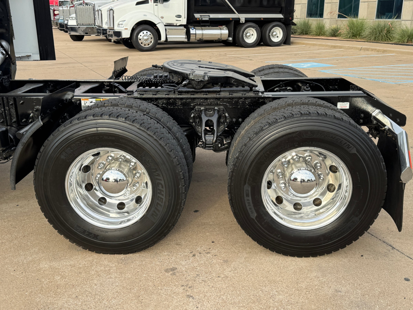 Kenworth T680 chassis with dual rear axles and polished chrome wheels, visible frame and fuel tanks in foreground.