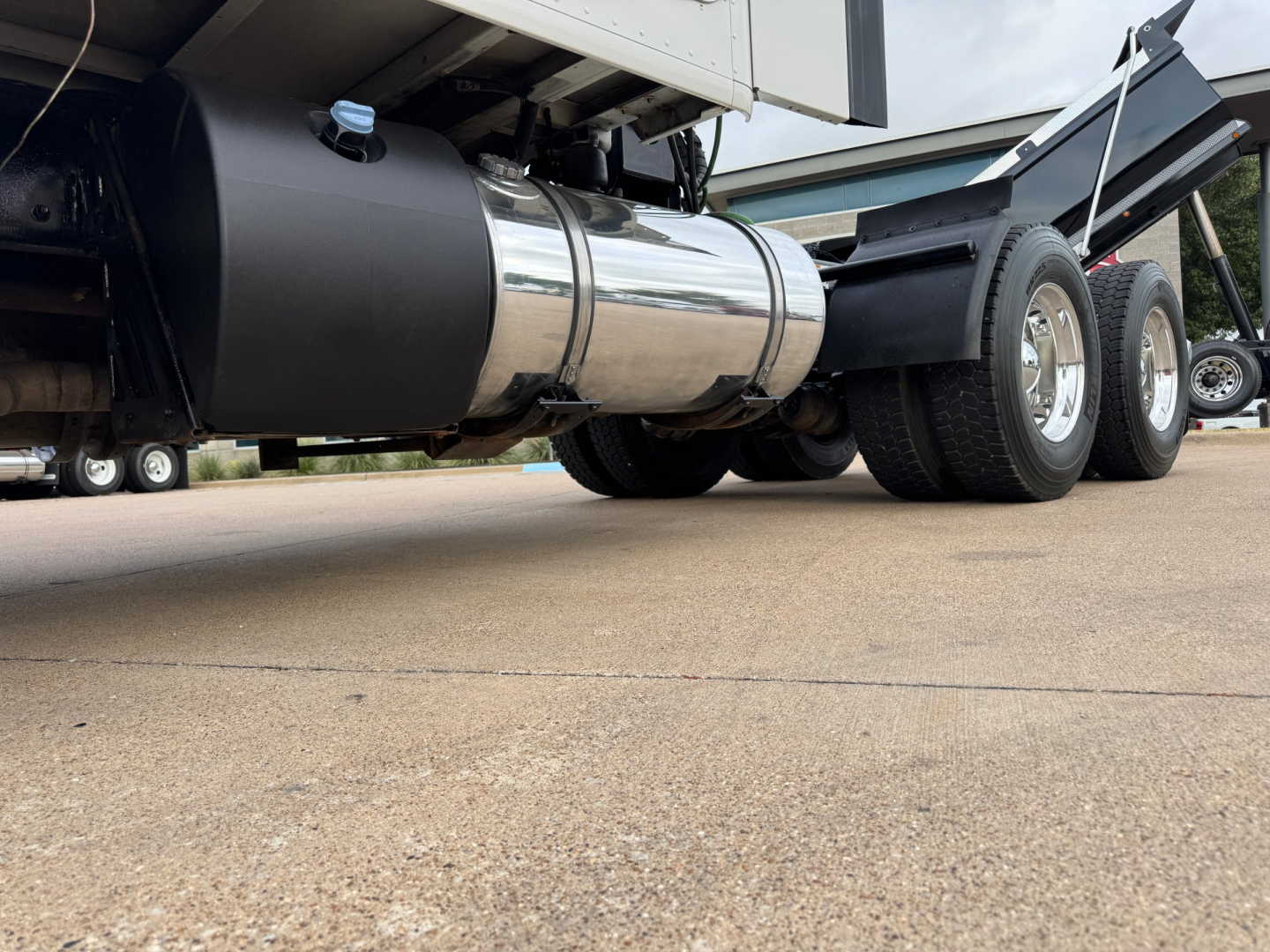 Kenworth T680 side view showing polished cylindrical fuel tank and dual rear axles under the trailer.