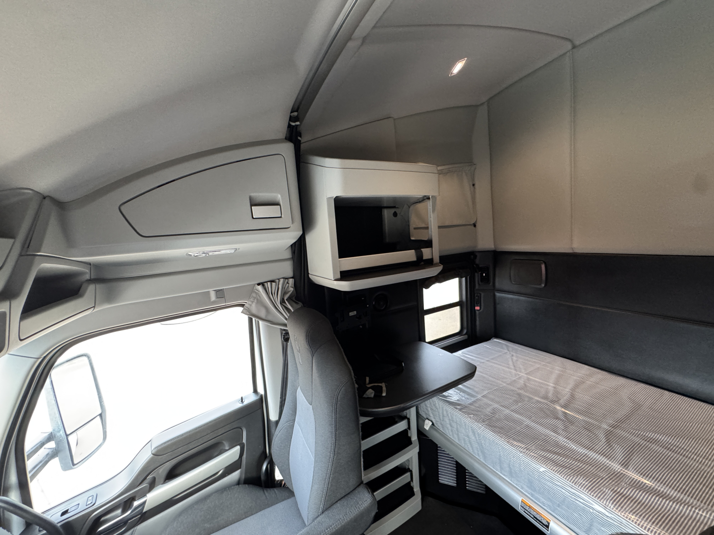 Kenworth T680 sleeper cab interior showing bunk bed with mattress, overhead storage, and small table; cabin area visible.
