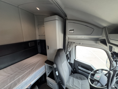 Kenworth truck interior cabin with sleeper berth and captain chair; dashboard and steering wheel visible.