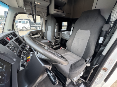 Cab interior of a Kenworth truck cab with steering wheel, driver's seat, and dashboard controls. Visible labels include truck interior panels and control buttons.