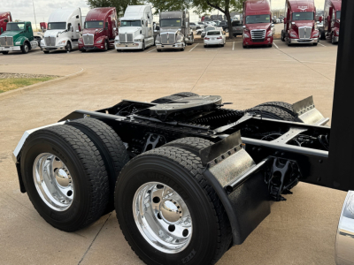 Kenworth T680 chassis with dual rear axles and chrome wheels, showing frame rails and fuel/air lines in a truck lot.
