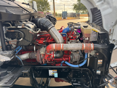 Kenworth T680 engine bay showing diesel engine with red intake manifold, blue and red hoses, black radiator frame, and various labels.