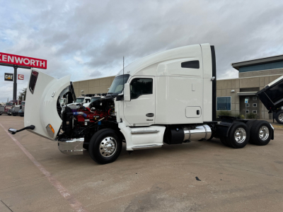 Kenworth T680 side view with hood open showing engine compartment and cab; visible text includes Kenworth logo on dealership and parts of the truck.