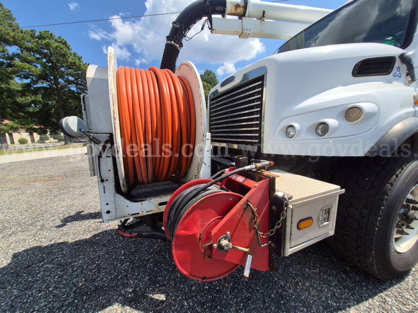 Freightliner M2 106 vacuum truck with large orange hose reel and reel stand near front wheel.