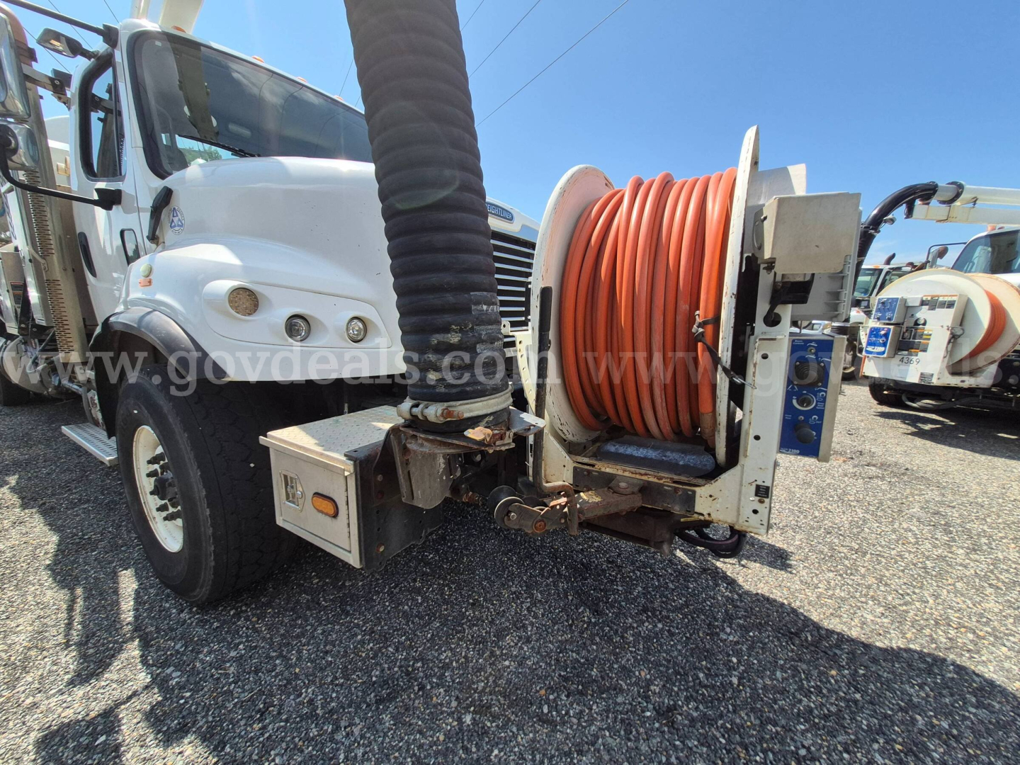 Freightliner M2 106 vacuum truck front quarter showing large orange hose reel and hose assembly on side with storage boxes and cab visible.