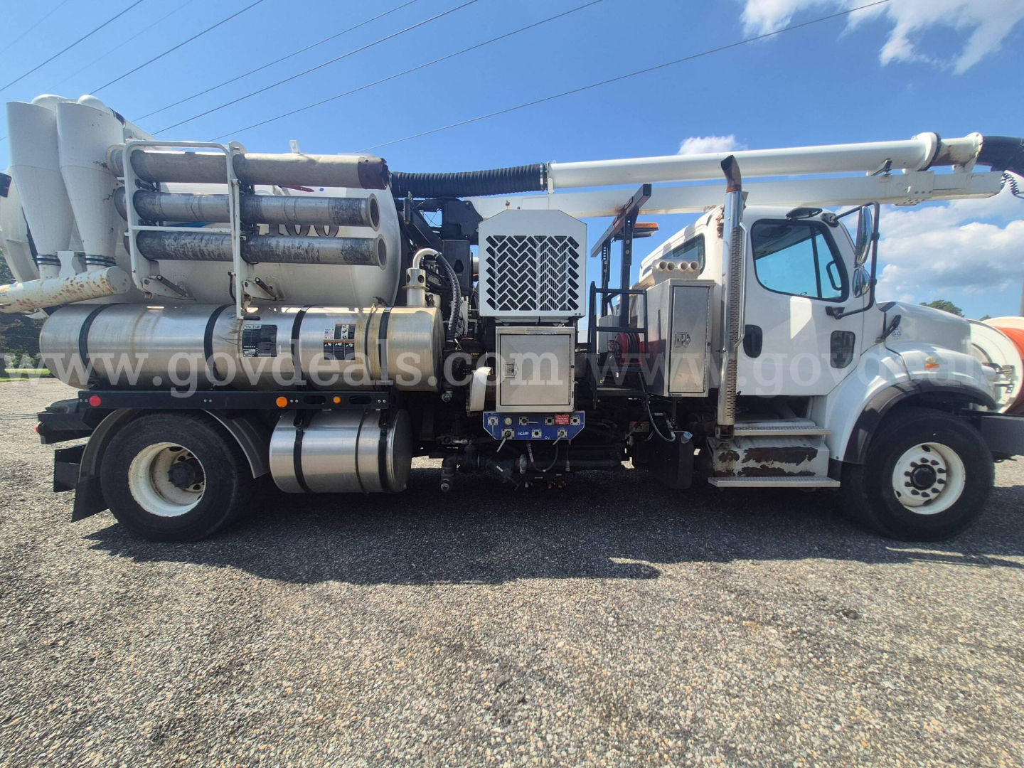 Freightliner M2 106 vacuum truck side view showing multiple cylindrical tanks and front cab with ladder steps.