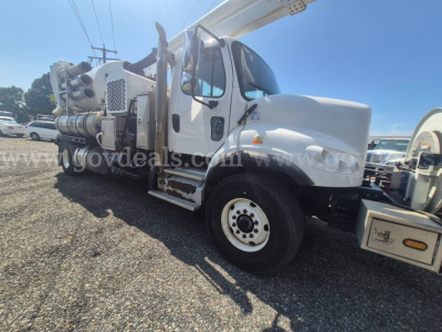 Freightliner M2 106 vacuum truck side view showing cab and boom, white exterior, large front wheel, equipment on rear body