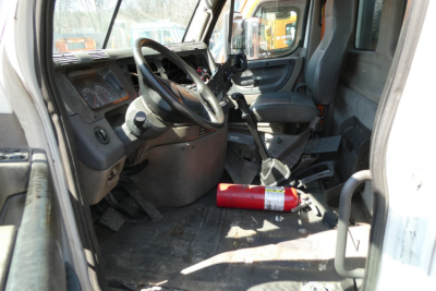 Cab interior of a Freightliner Cascadia 113 daycab showing steering wheel, dashboard, and seat with a red fire extinguisher on the floor.