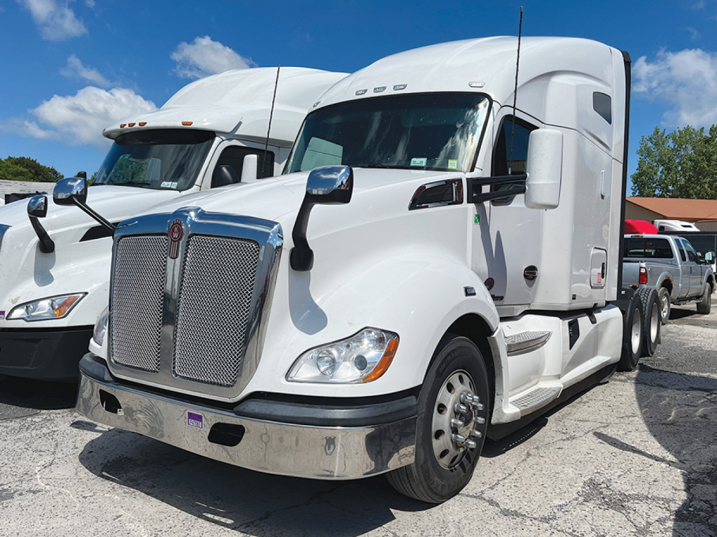 Kenworth T680 sleeper cab truck in a lot, front view with chrome grille and dual headlights.