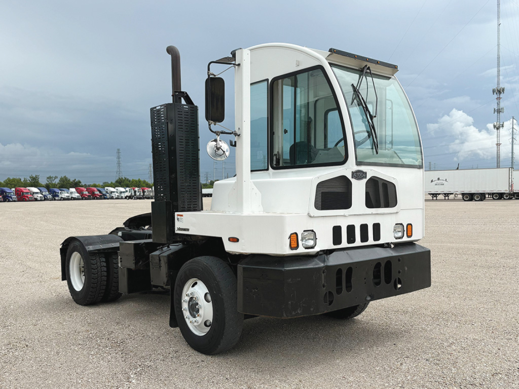 Autocar XSpotter yard truck cab with white body and black front bumper. Visible text on side includes manufacturer badges and controls; image shows truck in a large open lot.