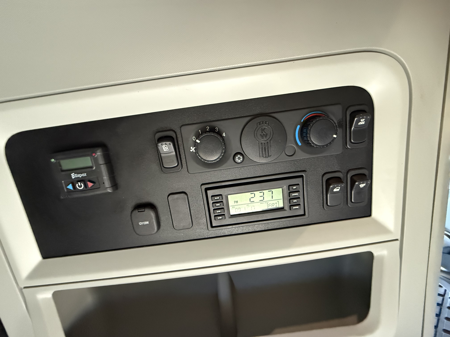 Dashboard panel of a Kenworth truck showing HVAC controls, switches, and a digital display. Visible text includes "KENWORTH" panel details and numeric gauge readings.