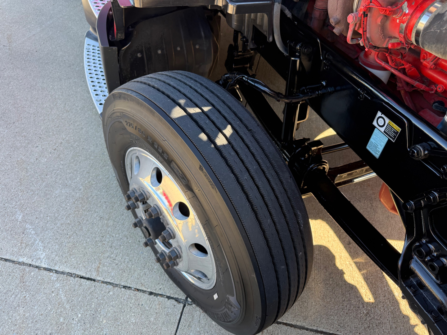 Kenworth T680 wheel and front suspension showing large steer tire and red engine block.”