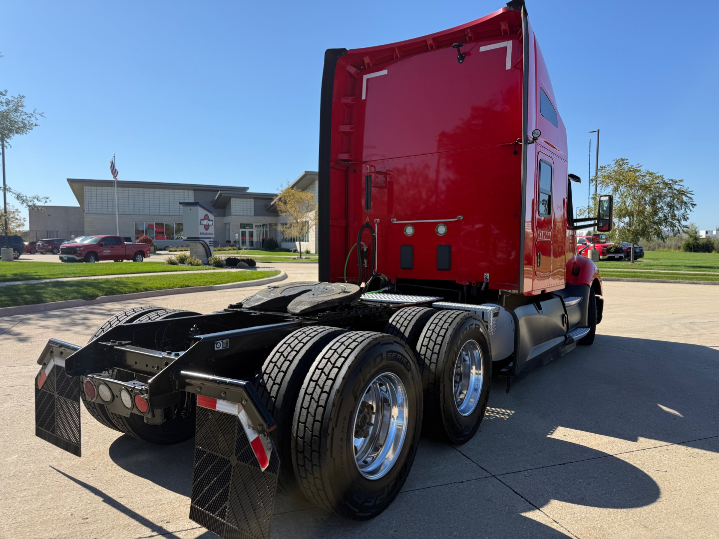 Kenworth T680 tractor rear view showing red sleeper cab and dual rear axles with chrome wheels.