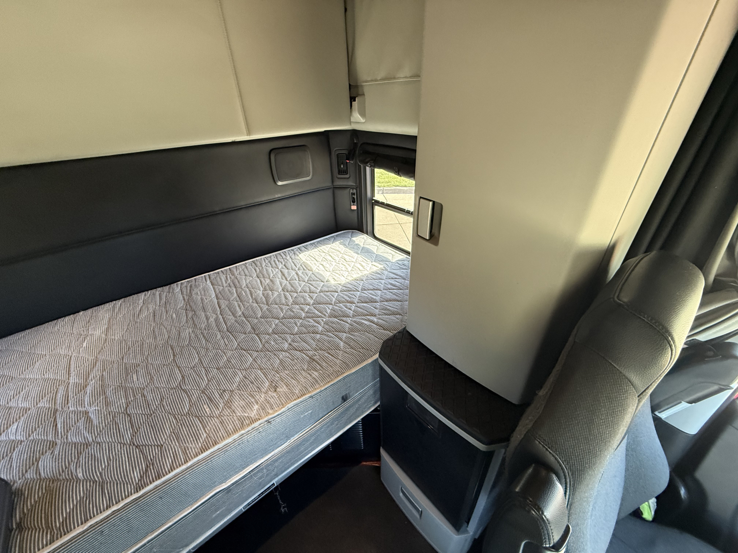 Kenworth T680 sleeper cab interior with a bed and side storage, clean light-gray upholstery.