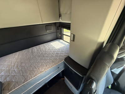 Kenworth T680 sleeper cab interior with a bed and side storage, clean light-gray upholstery.