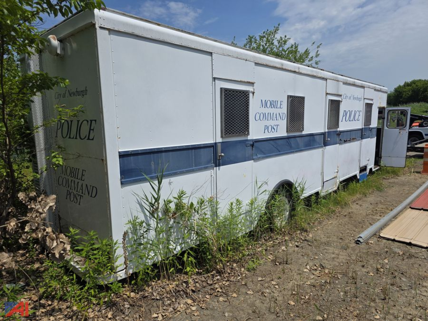 1986 International 1853 mobile police station truck with white body and blue stripe, labeled Mobile Command Post Police, side windows and rear entry, parked on dirt lot.