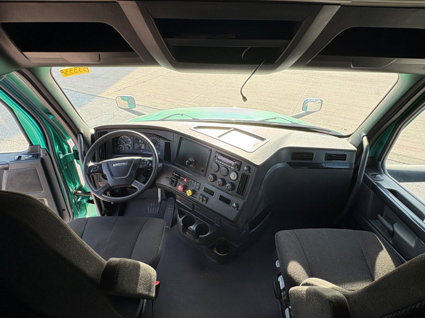 Truck cab interior of a Freightliner Cascadia 126 sleeper showing steering wheel, dashboard gauges, center console, and driver/passenger seats.