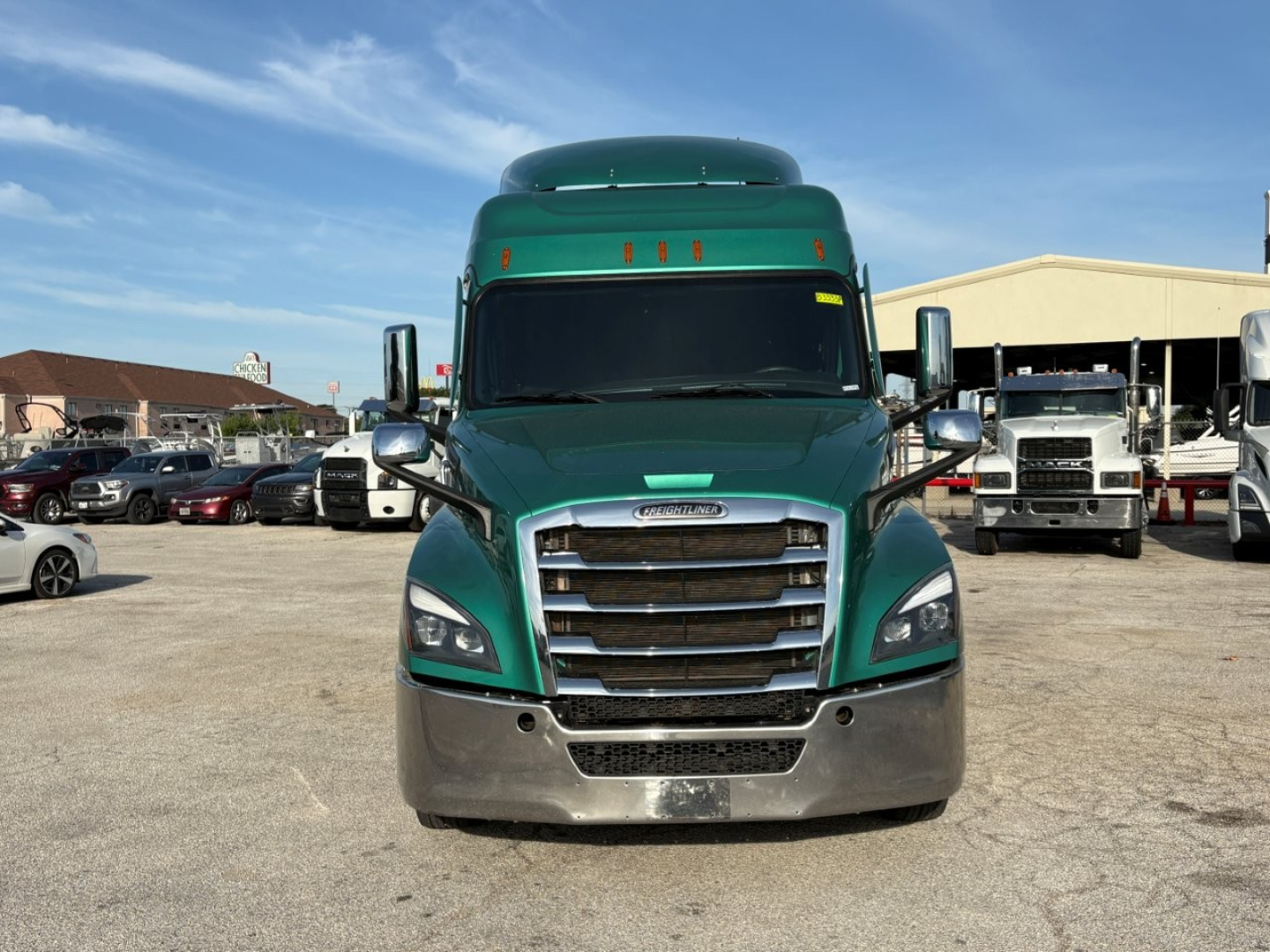 Freightliner Cascadia 126 truck by a dealership lot, front view showing green cab, large grille, silver bumper, and side mirrors.
