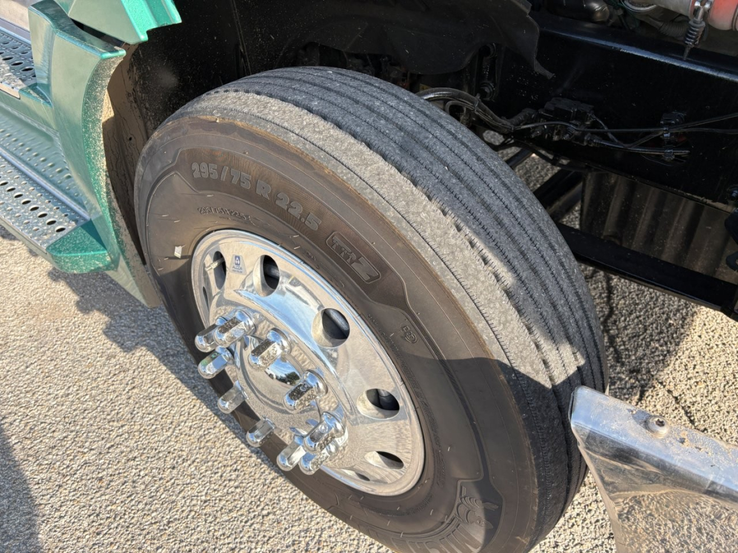 Front wheel and tire of a Freightliner Cascadia 126 sleeper tractor showing aluminum hub with lug nuts and tire sidewall markings 195/75R22.5.
