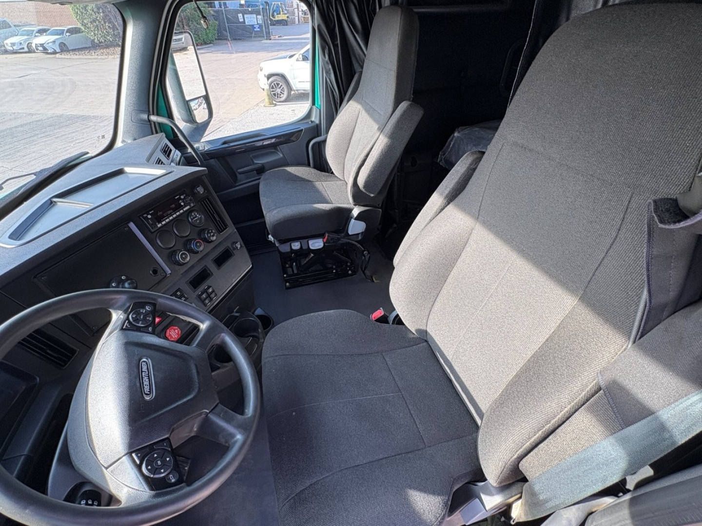 Cab interior of a 2023 Freightliner Cascadia 126 semi-truck showing driver seat, passenger seat, steering wheel, and dashboard with controls.